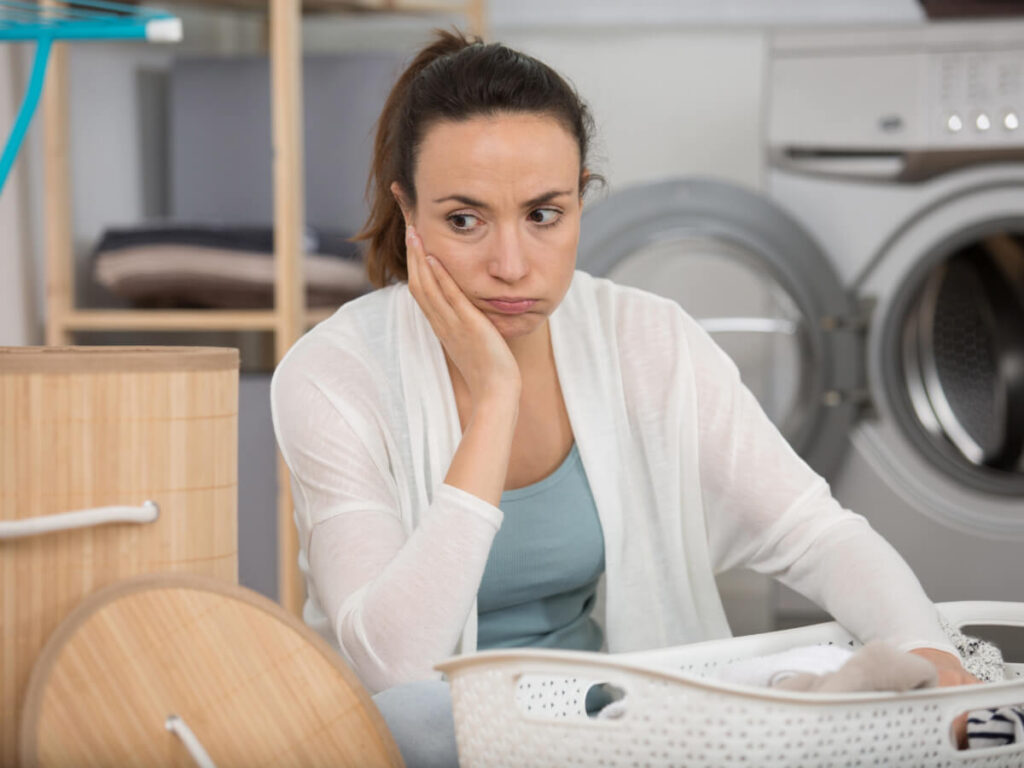 Frustrated woman with her chin in palm holding a laundry basket while sitting in laundry room