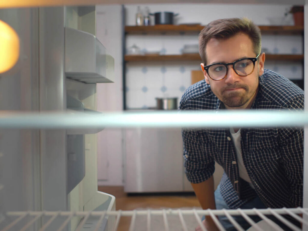 Frustrated man squatting and looking in fridge