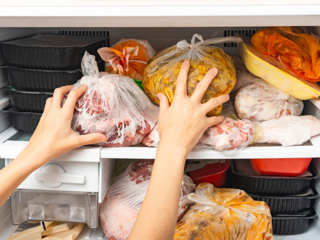 Close up image of person's hands in overflowing top freezer