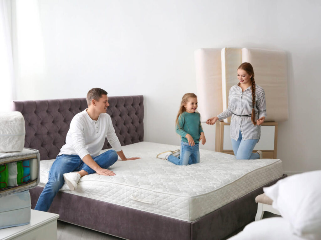 Parents and child sitting upright on bed smiling at one another