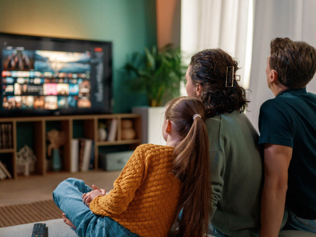 Back view of small family sitting in front of TV with a TV stand