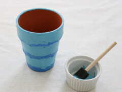 Wrap painters tape around the pot to serve as a guide while painting. Once straight lines have been added with equal spacing in between, paint the non-taped sections blue.