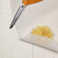 Secure pom-pom to the rug pad with the floss. Double knot the ends.