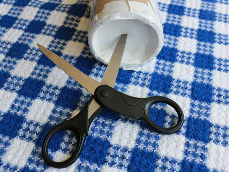 Close one end of the packing tube (using the plastic disc closure). Add tape to properly secure it shut. Use the end of your scissor to make a small hole in the end of the plastic tube. Scissors punching hole in paper