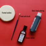 black food coloring, paintbrush, lemon extract, and frosted cookie