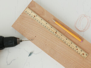 On the backside of your wood board, mark and drill two side-by-side starter holes, approximately one-fourth of the way down from the top of the board (vertically), and an inch in from each side.
