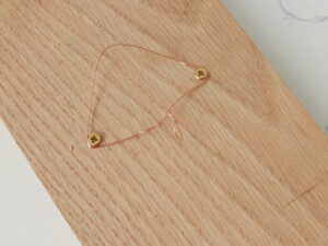 Just before the screws have been drilled in all the way, wrap a piece of hanging wire around the back of the screws and tie the wire ends firmly together.