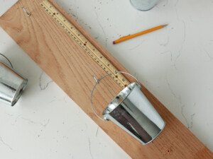 Before you add your plants to the tins, determine the spacing on the front side of your wood board. Make sure to keep an equal distance between each container, and use a pencil and ruler to mark the drill spots.