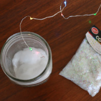 A bag of confetti sitting next to an open mason jar with string lights
