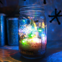 Miniature christmas trees and string lights in a mason jar